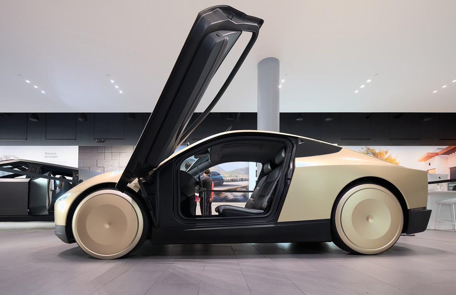 A Tesla Cybercab with its butterfly door open at a showroom. The two-seat robotaxi has no steering wheel or pedals.